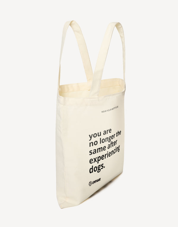 Natural canvas tote bag with the quote "You are no longer the same after experiencing dogs" by Empawr, shown from the side.