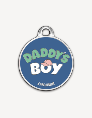 Empawr charm with the phrase "Daddy's Boy" in light green letters on a blue background, with a pink baseball cap graphic and silver trim. The brand name "EMPAWR" is at the bottom.
