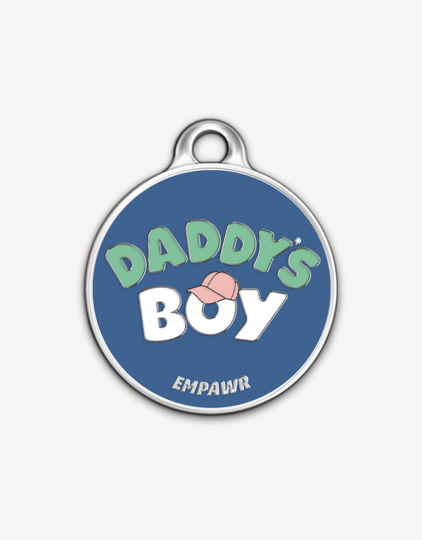 Empawr charm with the phrase "Daddy's Boy" in light green letters on a blue background, with a pink baseball cap graphic and silver trim. The brand name "EMPAWR" is at the bottom.