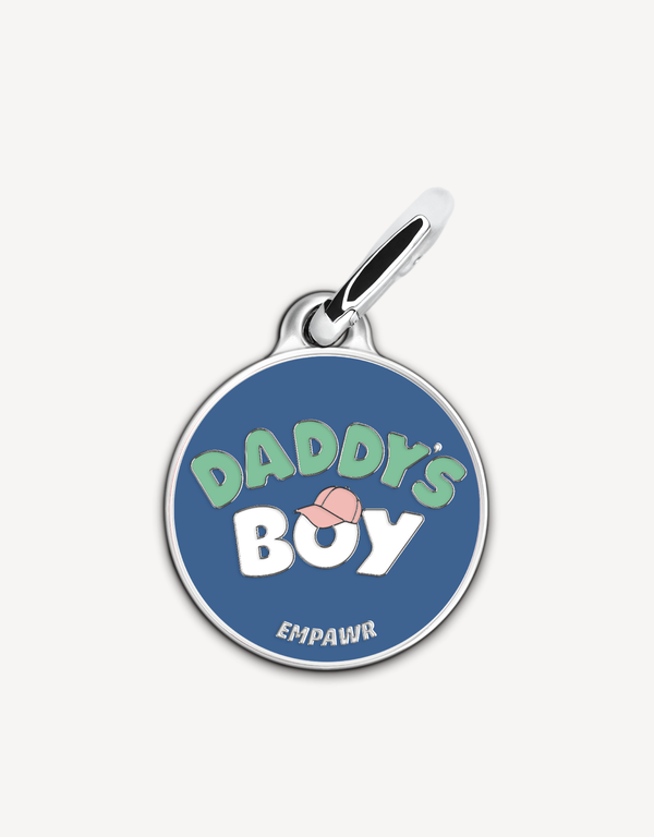 Empawr charm with the phrase "Daddy's Boy" in white letters on a blue background, with a pink baseball cap graphic and silver trim. The brand name "EMPAWR" is at the bottom.